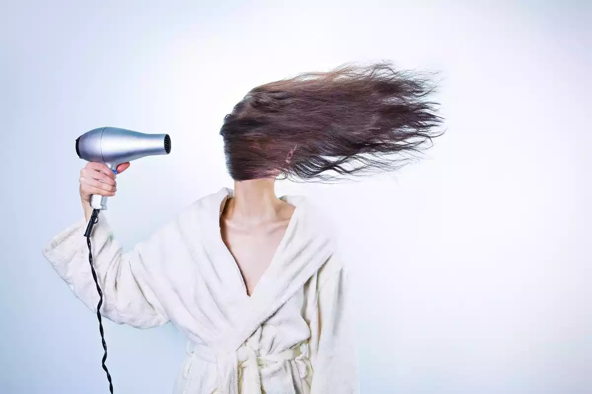 Una mujer recién duchada con un secador en la mano y el pelo hacia un lado