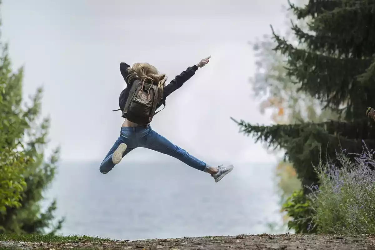 Una mujer saltando en medio del bosque con tejanos y la mochila puesta