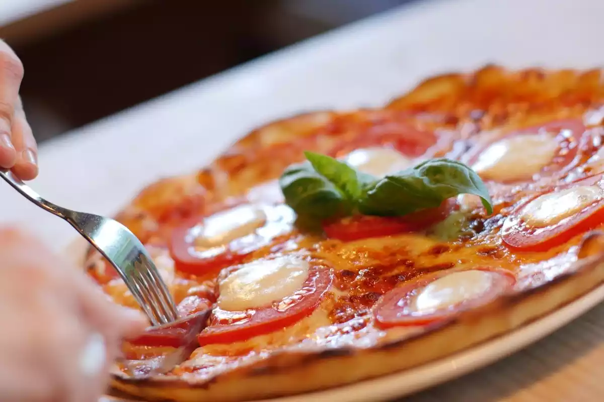 Una pizza con un tenedor recogiendo un trozo y albahaca en medio