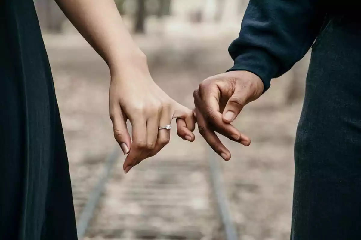 Una pareja en las vías de tren cogida por los dedos