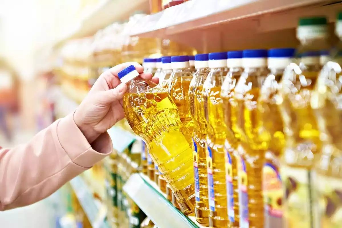 Botellas de aceite de girasol amarillo con una mano escogiendo una