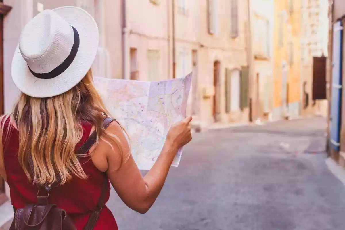 Mujer con sombrero mirando un mapa en el medio de una calle sin gente
