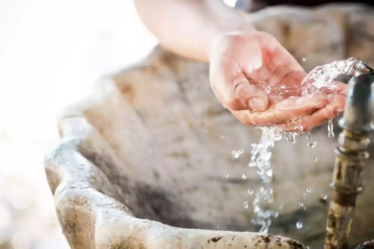 Una mano cogiendo agua de una fuente con forma de caracola