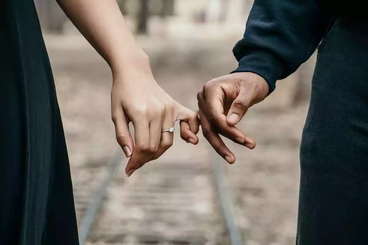 Una pareja cogida con los dedos de la mano sobre unas vías de tren