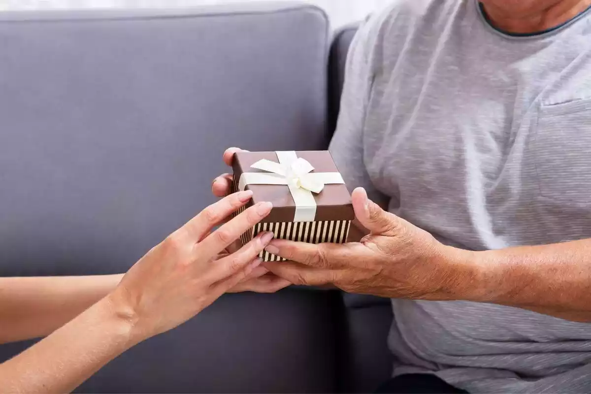Unas manos dándole un regalo a un padre sentado en un sofá