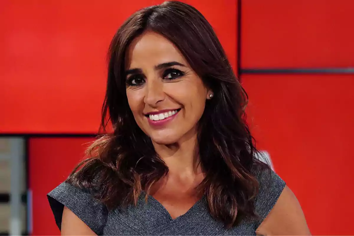 Una persona sonriendo frente a un fondo rojo.