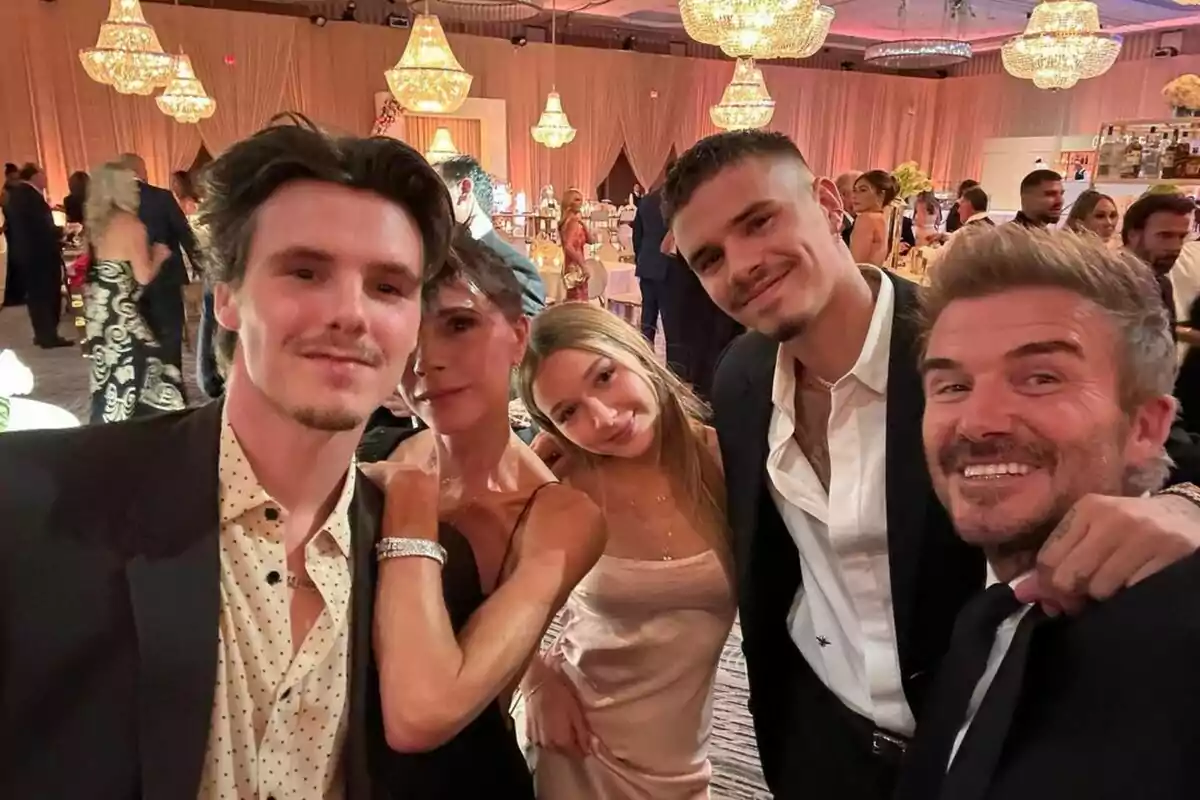 Un grupo de personas posando para una selfie en un evento elegante con lámparas de araña en el fondo. Un grupo de personas posando para una selfie en un evento elegante con lámparas de araña en el fondo.
