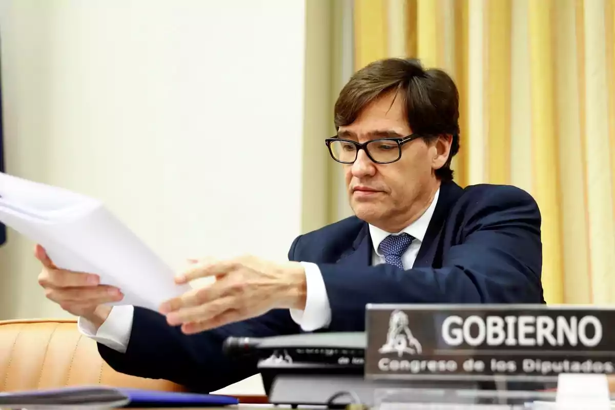 Un hombre con gafas revisa documentos en una oficina con un cartel que dice "Gobierno Congreso de los Diputados".