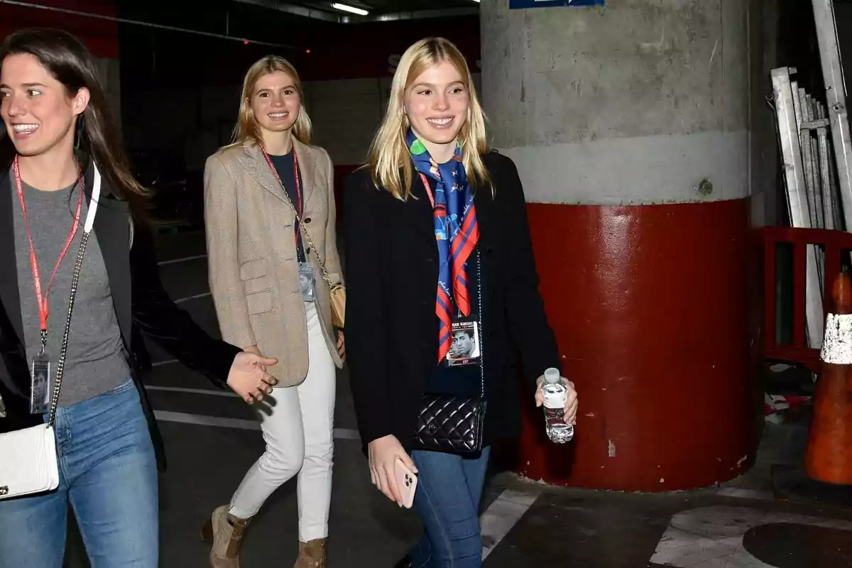 Cristina Iglesias, Victoria Iglesias y otra mujer caminando y sonriendo en un estacionamiento subterráneo, una de ellas lleva una botella de agua y un teléfono móvil en la mano. Cristina Iglesias, Victoria Iglesias y otra mujer caminando y sonriendo en un estacionamiento subterráneo, una de ellas lleva una botella de agua y un teléfono móvil en la mano.