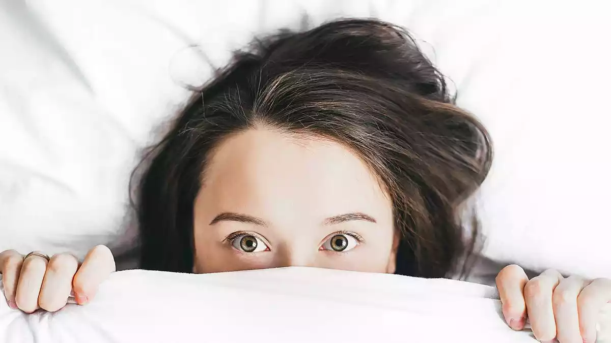 Imagen de una chica joven en la cama cubierta con una sábana