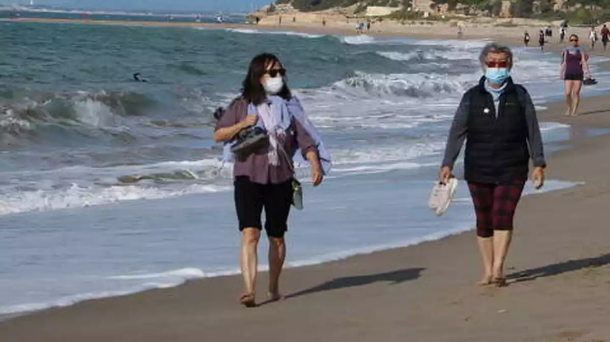 Pla general de dues dones amb mascareta caminant per la platja d'Altafulla en el primer dia permès per sortir a practicar esport.